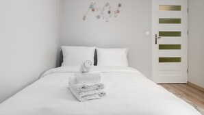 A neatly made bed with white linens and a folded towel on top, a wall-mounted decorative string, and a white door with horizontal panels. - Krowoderskich Zuchów Standard Studio (Kraków)