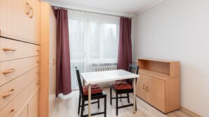 A small room with a white table, two chairs, a wooden cabinet, and a window with curtains. - Krowoderskich Zuchów Standard Studio (Kraków)