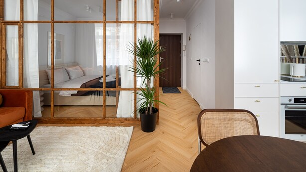 A modern living room with a wooden-framed sliding door, a white sofa, a dining table, and a kitchen area with white cabinets and a built-in oven. - Hoża Modern Apartment (Warszawa)