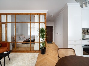 A modern living room with a wooden-framed sliding door, a white sofa, a dining table, and a kitchen area with white cabinets and a built-in oven. - Hoża Modern Apartment (Warszawa)
