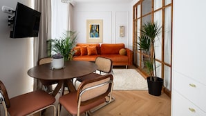 A modern living room with a sofa, a dining table with chairs, a TV mounted on the wall, and a large window with curtains. - Hoża Modern Apartment (Warszawa)