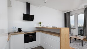 A modern kitchen with white cabinets, a wooden countertop, a black stove, and a black range hood. There is a small table with a vase and a magazine.