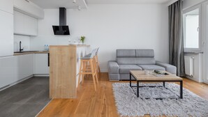 A modern living space with a kitchen, grey sofa, wooden dining table, and a fluffy rug.