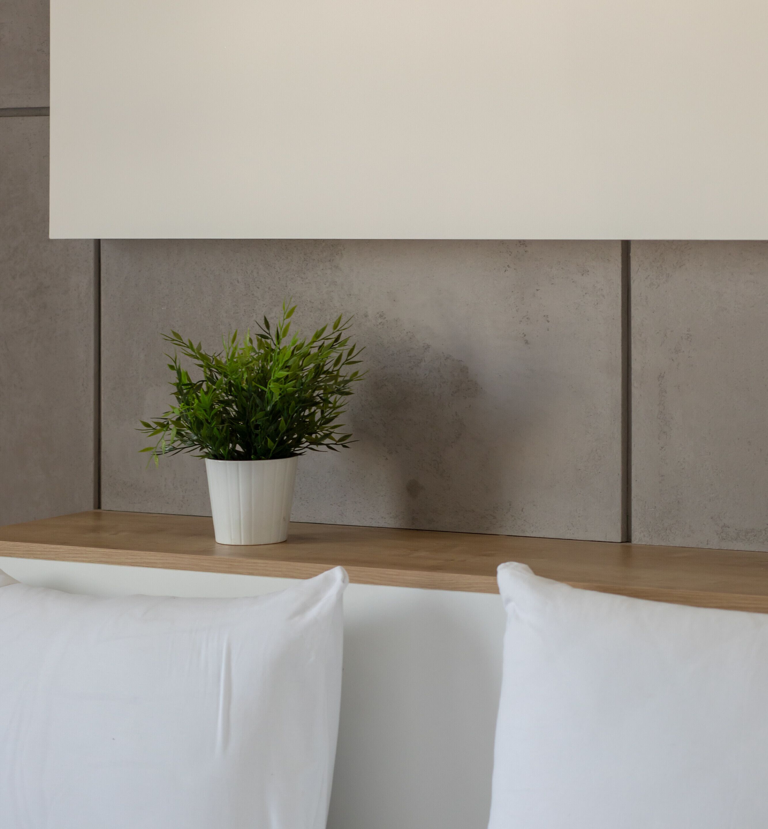 Un interior moderno con una mesa de madera, sillas blancas, una planta en maceta blanca y una pared gris con textura.