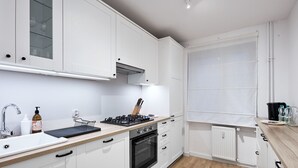 Una cocina moderna con armarios blancos, una estufa negra, un lavamanos y una ventana con persianas.