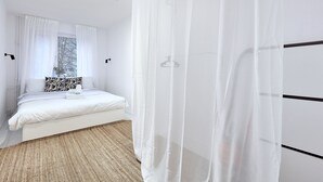 Un dormitorio moderno con una cama, cortinas blancas y vistas a árboles.