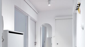 Un pasillo con paredes blancas, piso de madera y una puerta con espejo.