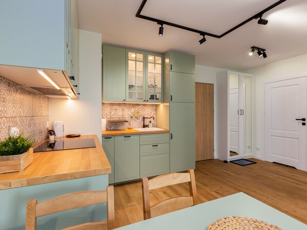 A modern kitchen with light green cabinets, a wooden countertop, and a dining area with a table and chairs.