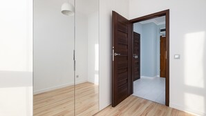 Ein Zimmer mit Holzboden, einer Glastrennwand und einer Holztür, die in ein weiteres Zimmer führt.