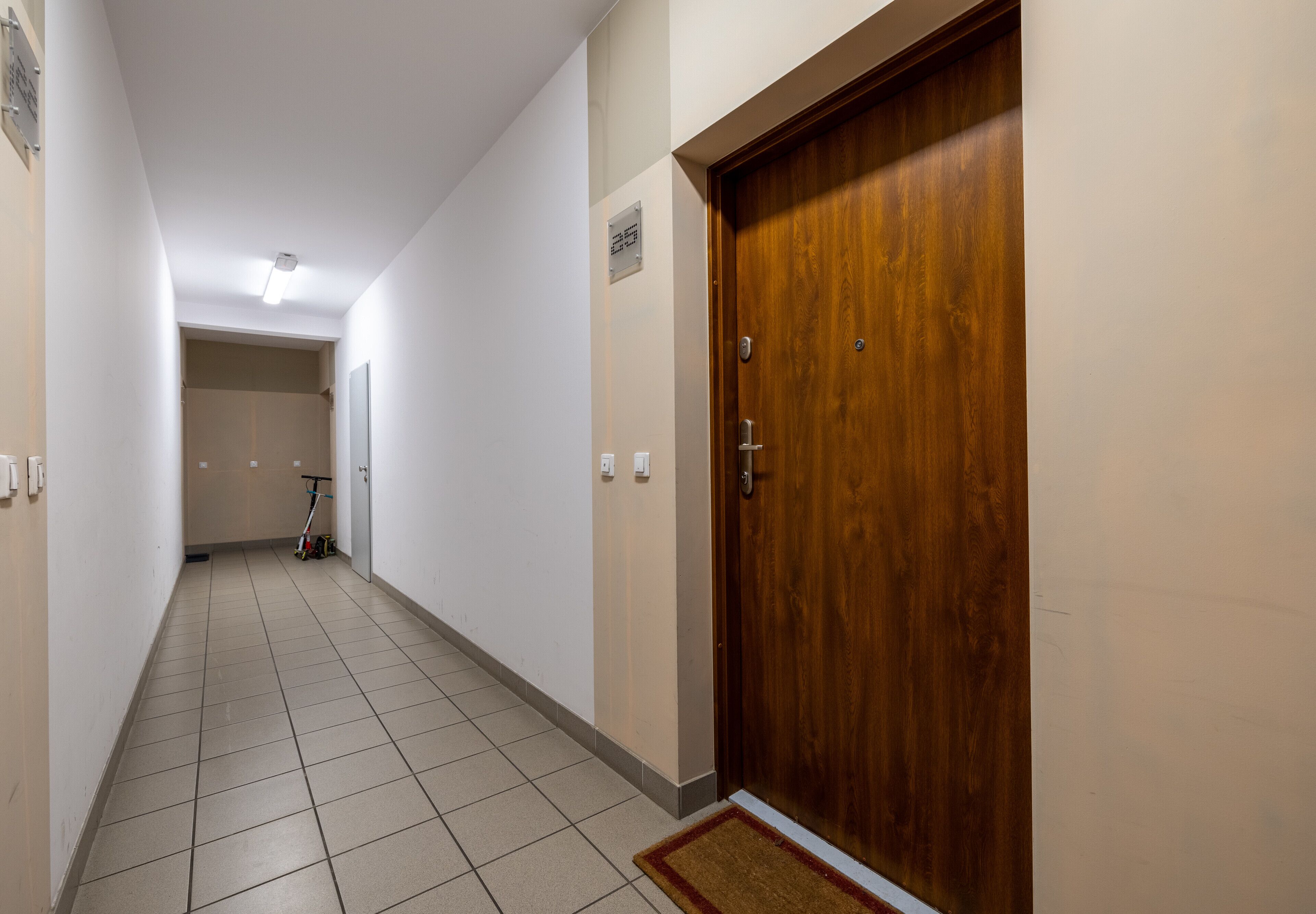 A hallway with a wooden door, tiled floor, and a scooter parked in the distance.