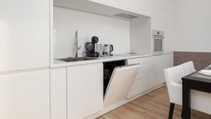 Eine moderne Küche mit weißen Schränken, einem Geschirrspüler, einer Kaffeemaschine und einem Backofen.