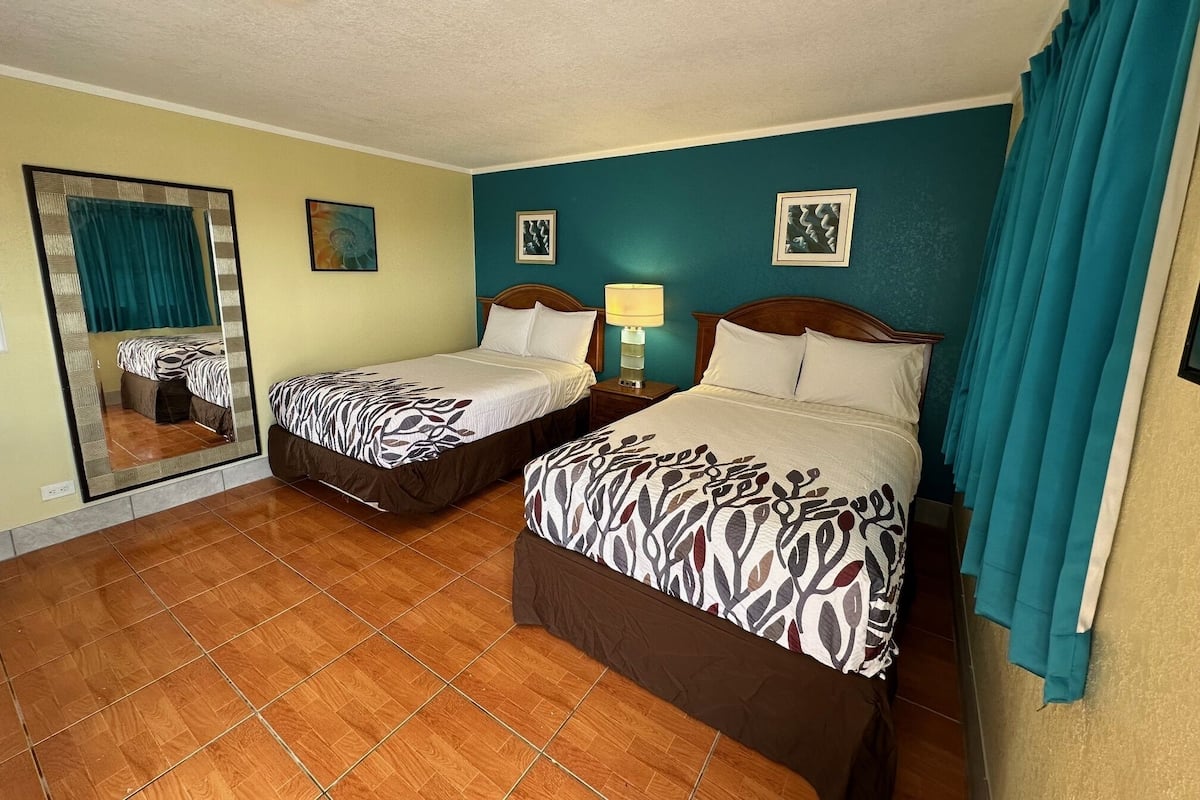 A hotel room with two beds, a large mirror, and a nightstand with a lamp.