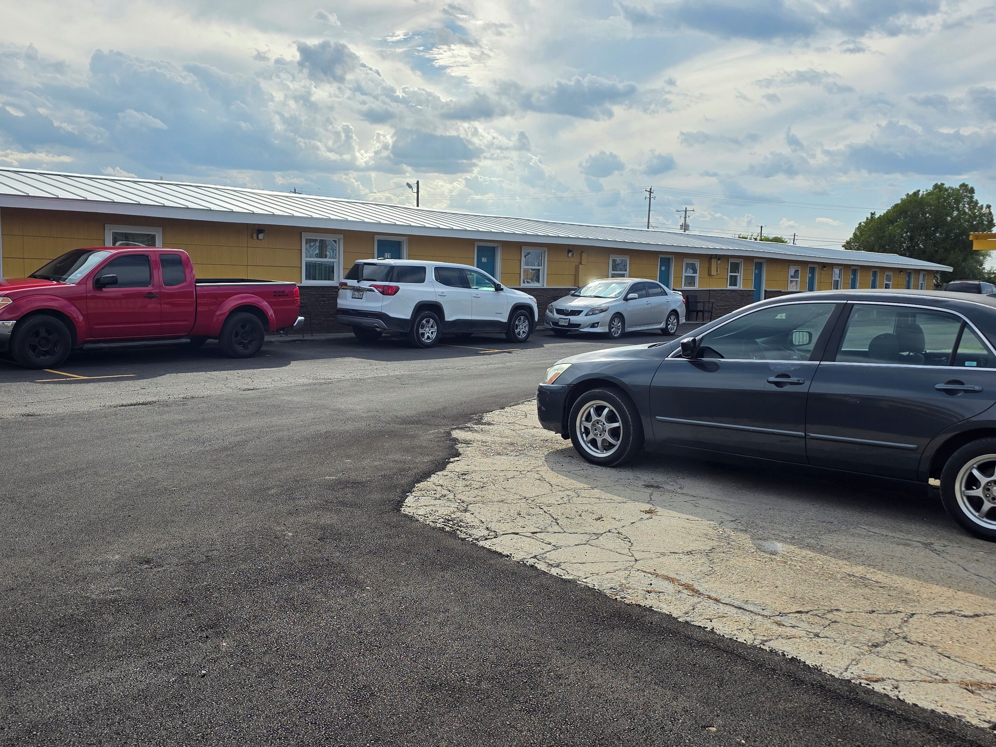 Um estacionamento com vários veículos, incluindo uma caminhonete vermelha, um SUV branco e um sedan cinza.