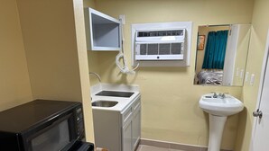 A compact kitchen with a microwave, oven, sink, and a white pedestal sink. - Royal Inn (Kenedy)