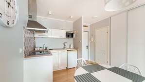 A modern kitchen with white cabinets, a stainless steel range hood, a microwave, and a dishwasher. There is a dining table with chairs in the foreground.