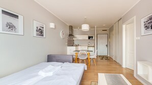 A modern hotel room with a bed, a small dining table, and a kitchenette.