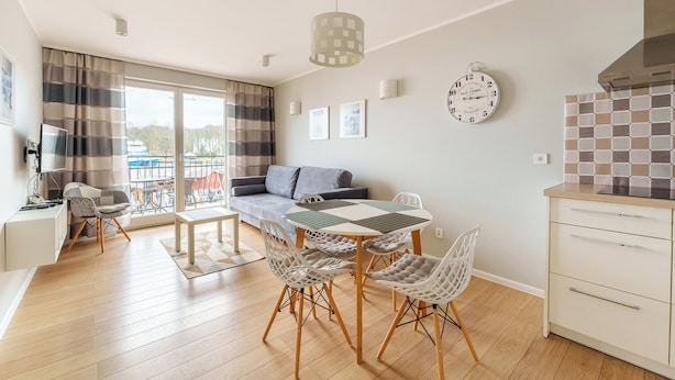 A modern living room with a dining area, a sofa, a TV, and a kitchen area with a stove.