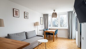 A modern living room with a grey sofa, a wooden dining table, and a TV. - Plac Zawiszy Cosy Apartment (Warszawa)