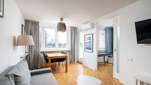 A modern living room with a grey sofa, a dining table with chairs, a white coffee table, and a TV mounted on the wall. - Plac Zawiszy Cosy Apartment (Warszawa)