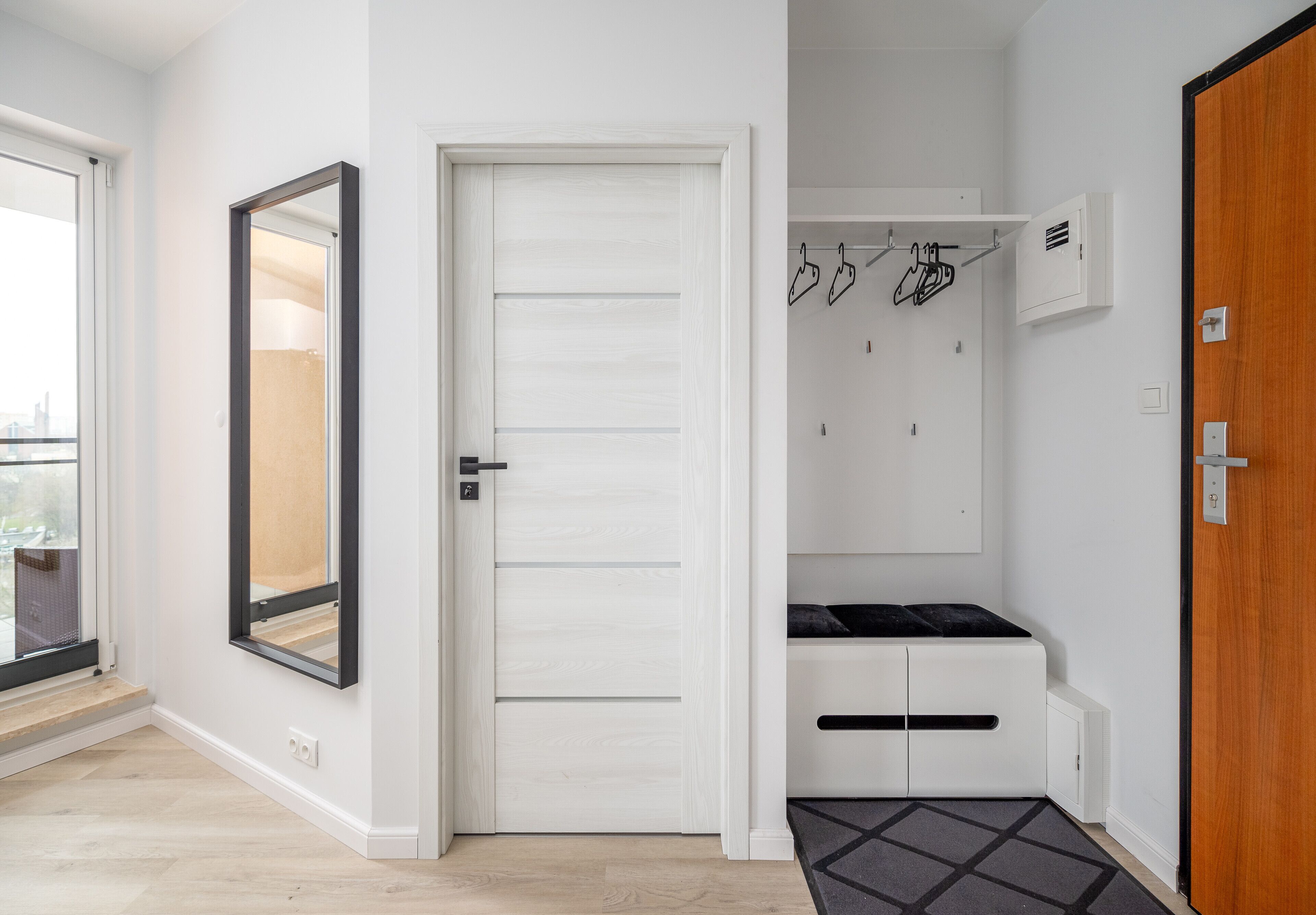 Un couloir avec une porte blanche, un porte-manteau et un banc.
