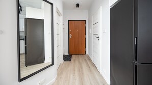 Een gang met een houten deur, een zwarte koelkast en een grote spiegel aan de linker muur.