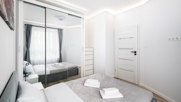 Een moderne slaapkamer met een groot bed, nachtkastje, spiegel en een kledingkast.