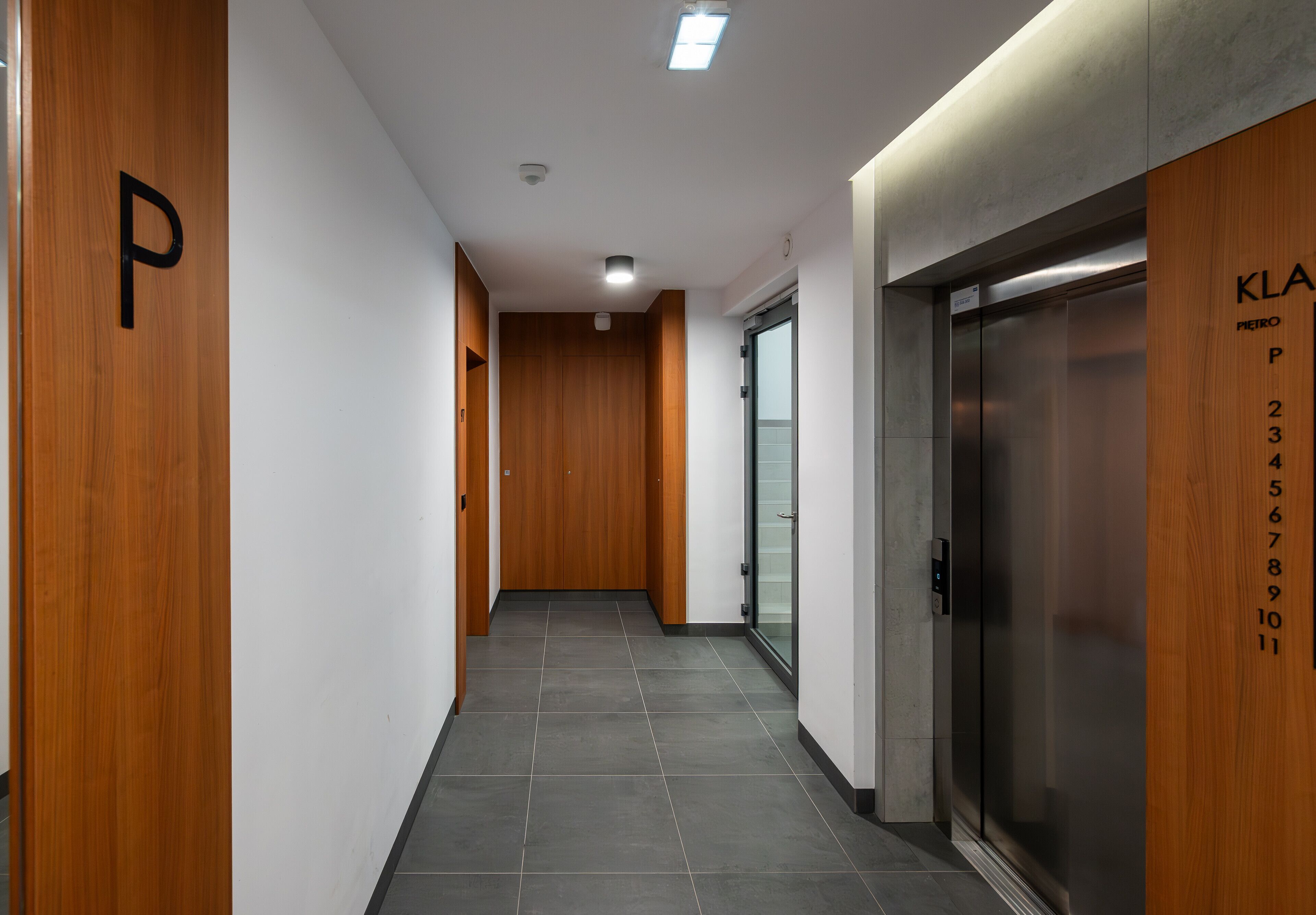 A modern hallway with wooden paneling, a tiled floor, and an elevator with numbered doors.