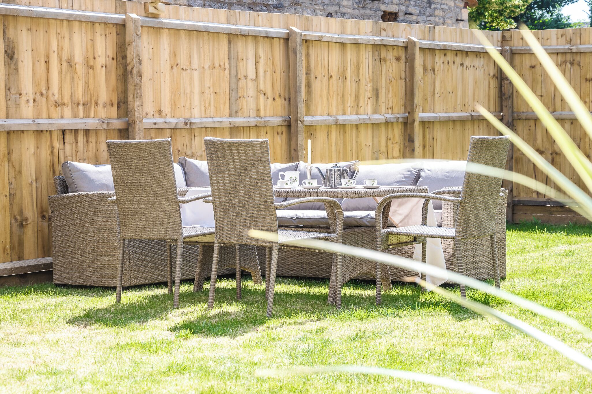 Une terrasse dotée de meubles en osier et d’une table préparée pour le thé, le tout entouré d’une clôture en bois.