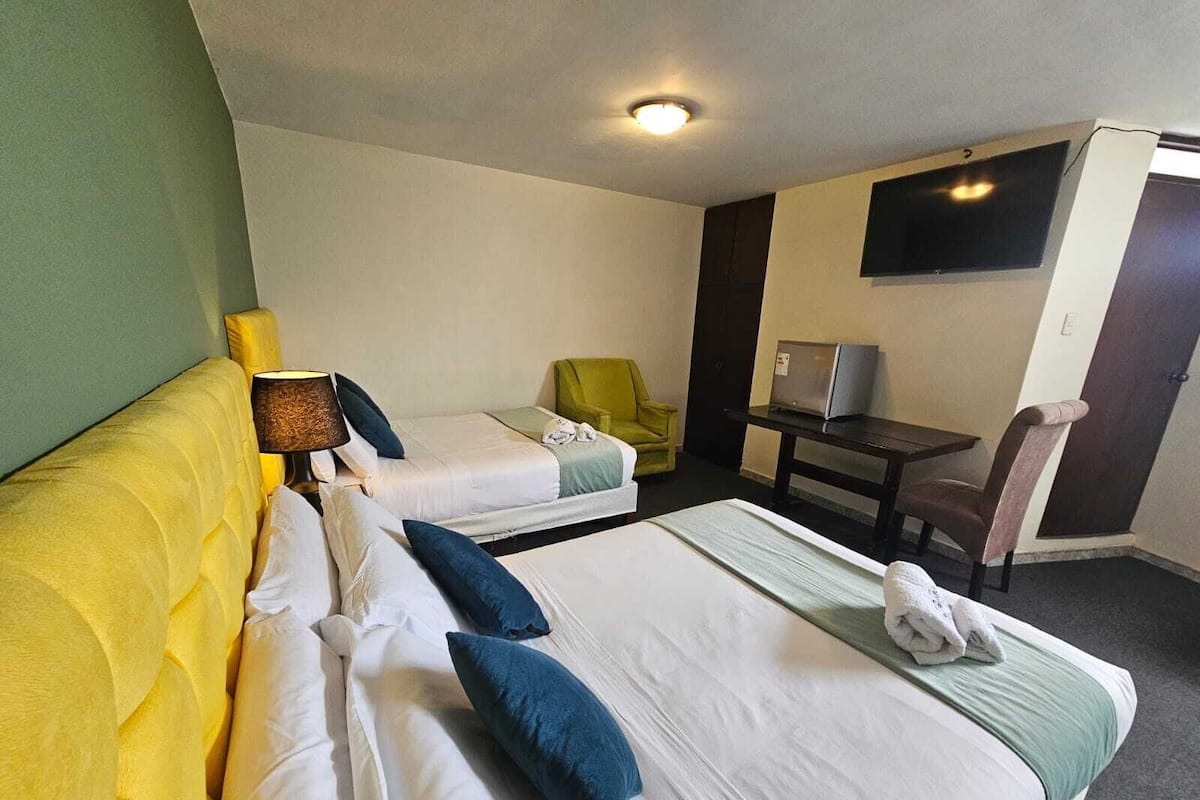 A hotel room with two beds, a desk, a chair, a television, and a lamp.