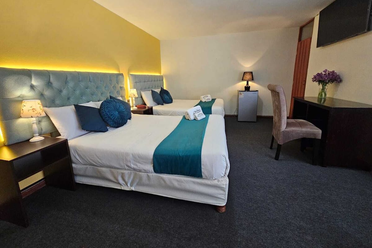 A hotel room with two beds, a desk, a chair, and a TV on the wall.