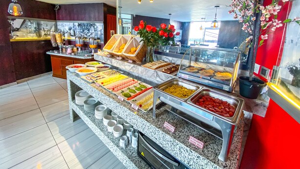 A buffet area with various food options, a mirror, and a vase with red flowers. - Hotels Collect A. Monet (Arequipa)
