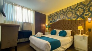 A hotel room with a large bed, a desk, a chair, a nightstand, and a wall with patterned wallpaper. - Hotels Collect A. Monet (Arequipa)