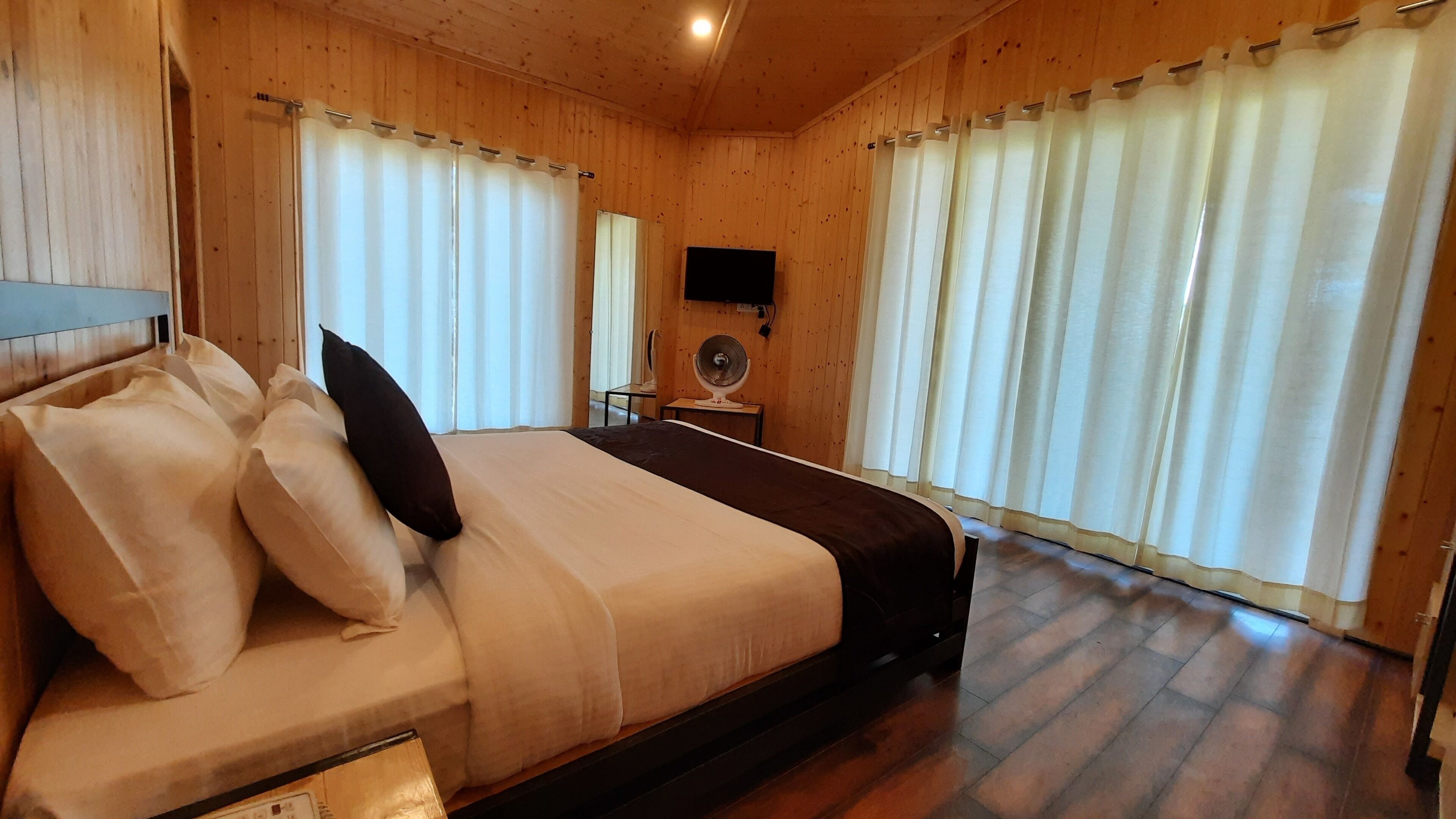 Ein Schlafzimmer mit Holzvertäfelung, einem Bett, Kissen, einem Flachbildfernseher und einem Standventilator.