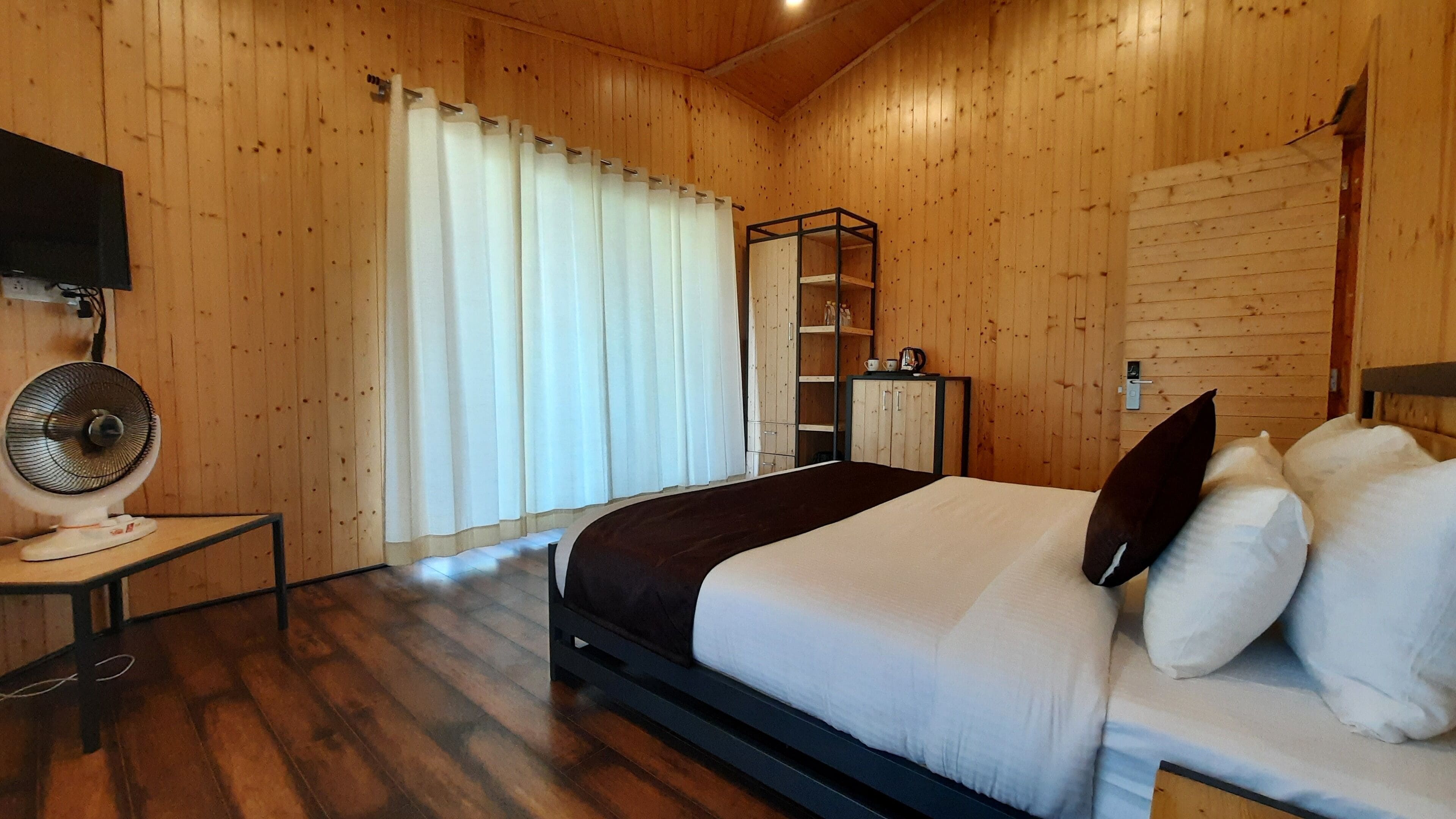 Een slaapkamer met houten lambrisering, een bed, een ventilator, een kledingkast en een spiegel.