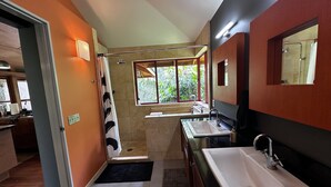 A modern bathroom with a shower, two sinks, and a large window providing natural light.