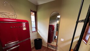 A compact kitchen with a red Galanz refrigerator, a black trash bin, and a wooden floor.