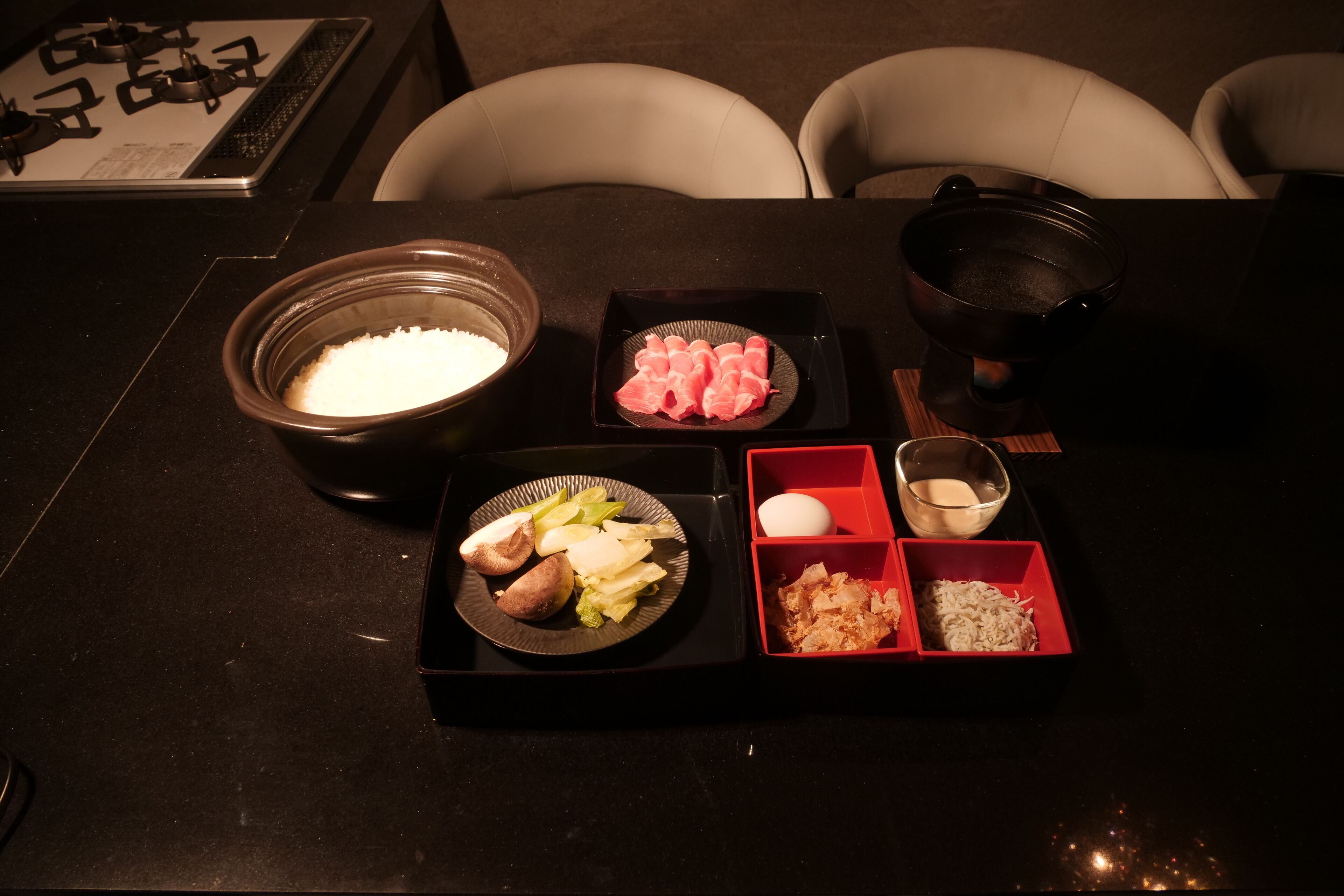 Una mesa con varios alimentos, incluyendo un bol de arroz, un plato con verduras, un plato de sashimi y un cuenco pequeño de sopa.