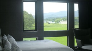 A bedroom with a bed, a chair, and large windows offering a view of a green landscape and distant buildings. - PLUFINO RESORT VILLA (Ise)