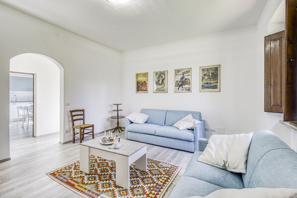 Un salon avec un canapé bleu, une table basse, un tapis à motifs et trois affiches accrochées au mur.