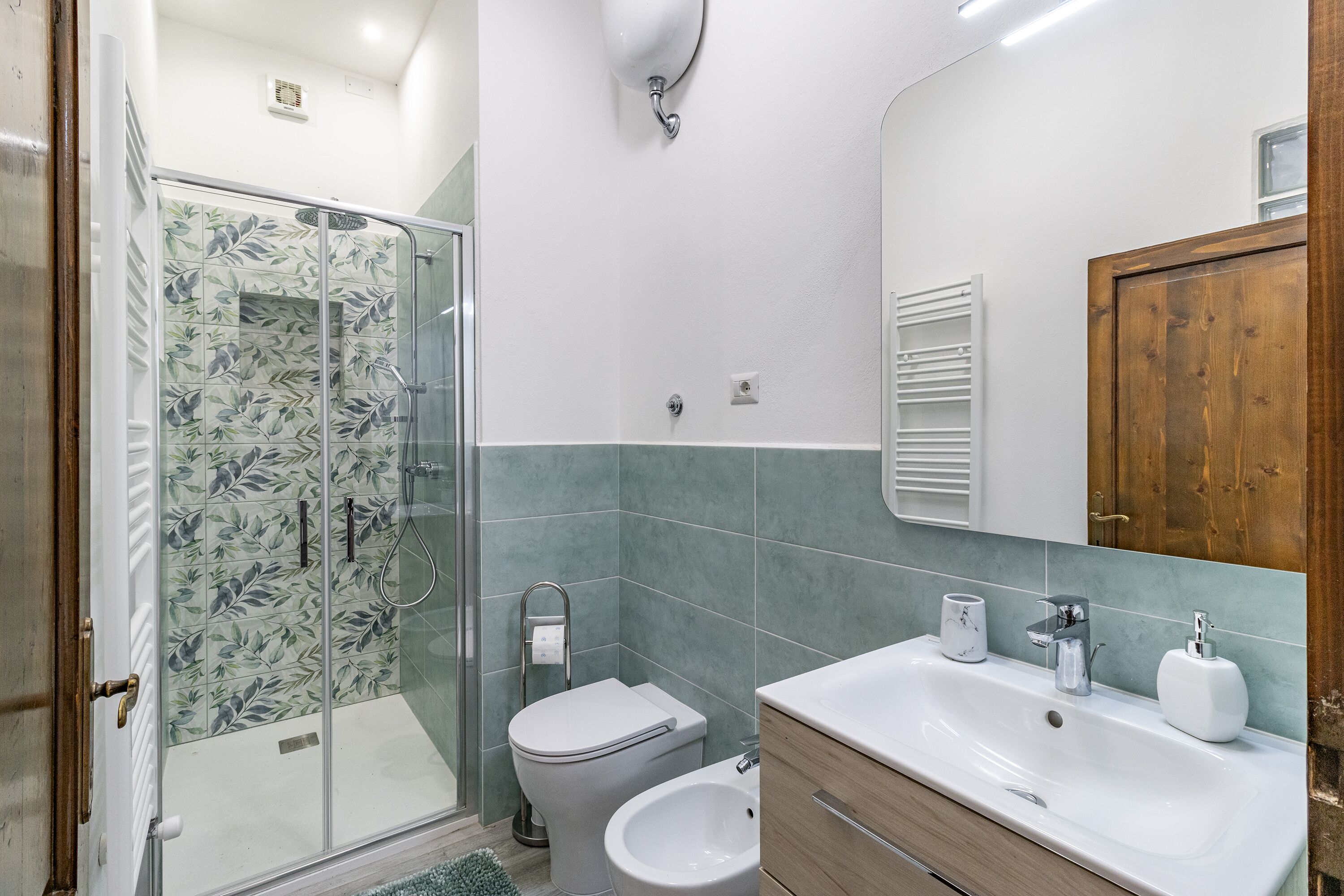 Ein Badezimmer mit Duschkabine aus Glas, Toilette, Bidet, Waschbecken mit Spiegel und Holzschränken.