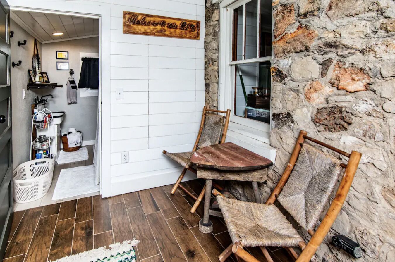 Un interior rústico con pared de piedra, sillas de madera y una pequeña mesa de madera.