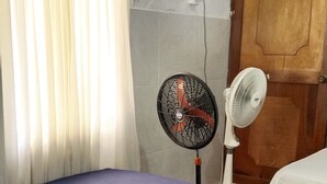 A bedroom with a bed, two fans, a wooden door, and a curtain. - shanty guest house (Cartagena)