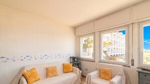 Une pièce avec deux canapés, une petite table et une vue sur les immeubles à travers de grandes fenêtres.