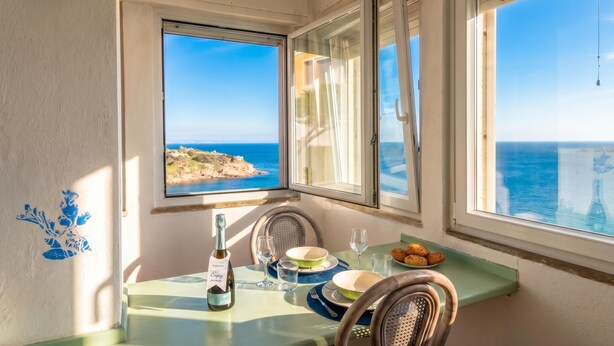 Un coin repas avec une table dressée pour deux personnes, une bouteille de vin et une vue sur la mer.