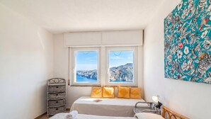 Une chambre avec deux lits, une vue sur des falaises, un meuble de rangement en osier et un tableau.