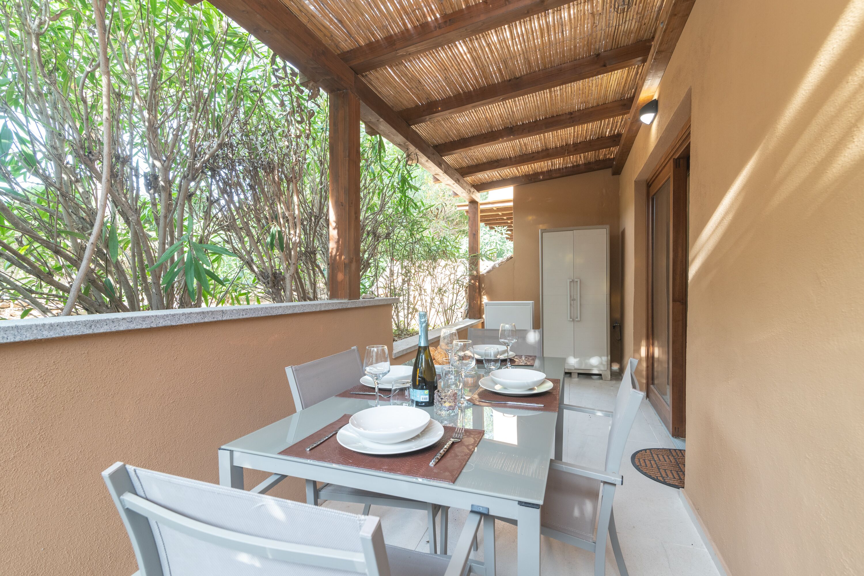 An outdoor dining area with a table set for two, surrounded by chairs, and a bottle of wine on the table.