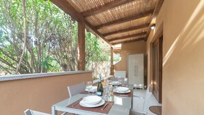 An outdoor dining area with a table set for two, surrounded by chairs, and a bottle of wine on the table. - White Sand House, Portisco, Italy (Portisco)