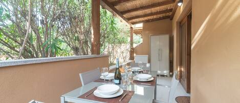 An outdoor dining area with a table set for two, surrounded by chairs, and a bottle of wine on the table.