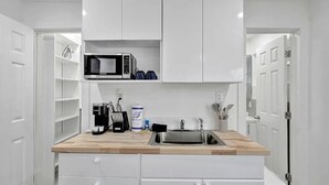 A compact kitchen with white cabinetry, a microwave, a coffee maker, and a sink. - Bright Studio | Walk to Pompano Beach & Pier (Pompano Beach)