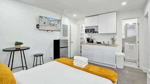 A compact hotel room with a bed, a small kitchenette, a dining area, and a bathroom.